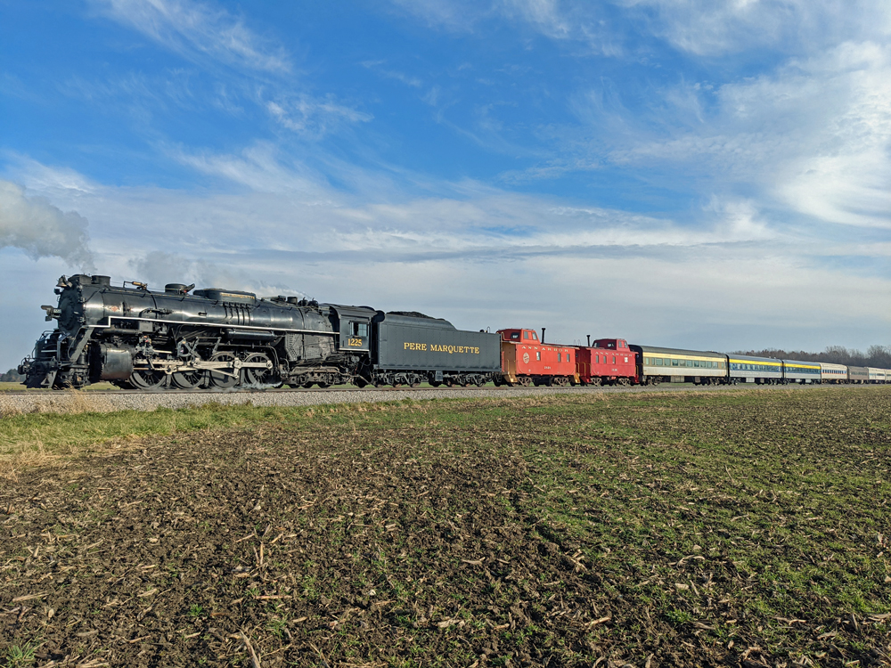 A steam engine crosses behind a harvested field in the fall