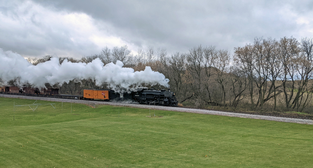 A steam locomotive hauls a freight train across a field