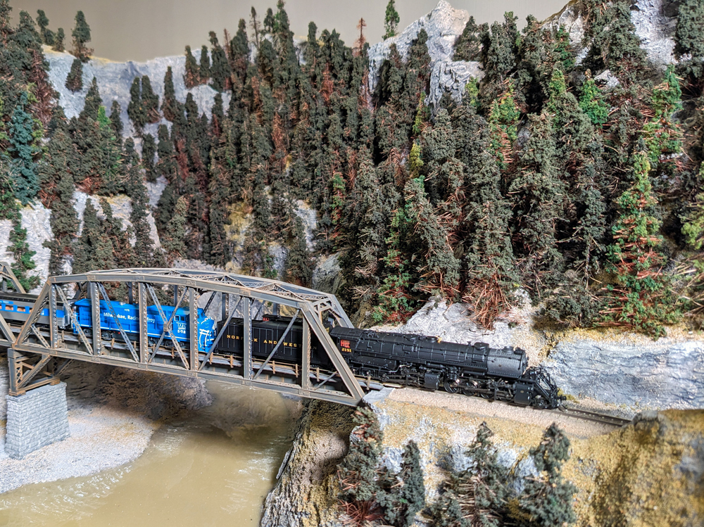 Model steam locomotive and diesel locomotive cross over a bridge
