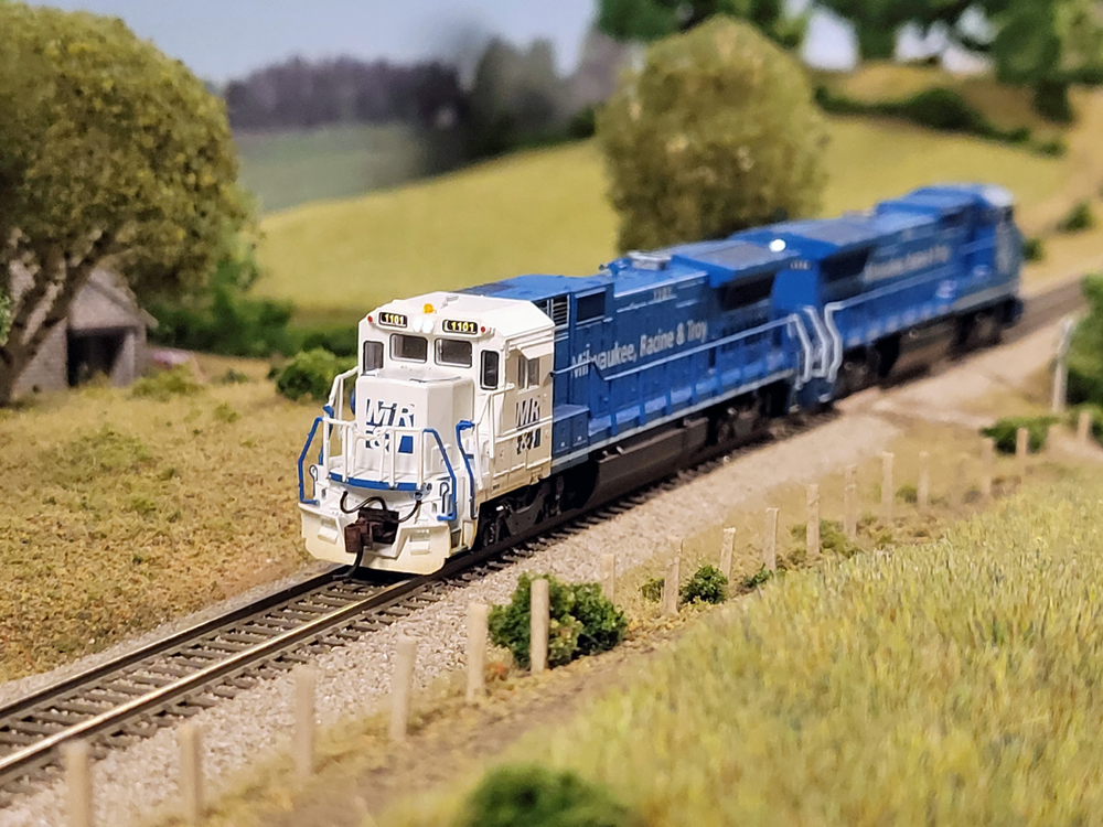 Two model locomotives pass a field.