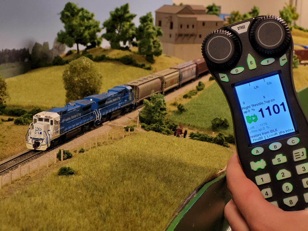A man holds a model railroad throttle next to a model freight train.