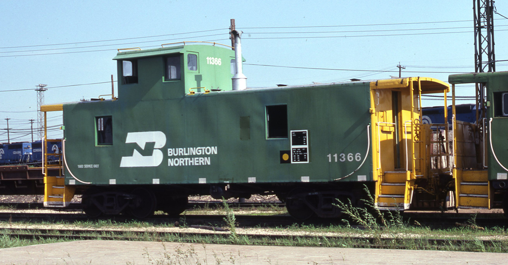 Color photo of offset-cupola caboose in yard.