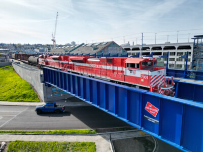 Red and white diesel locomotives pull freight train over blue bridge.