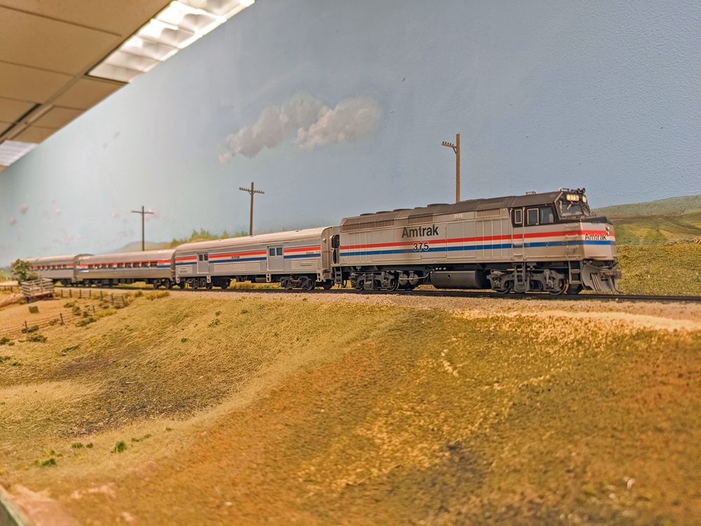 A model passenger train passes a field.