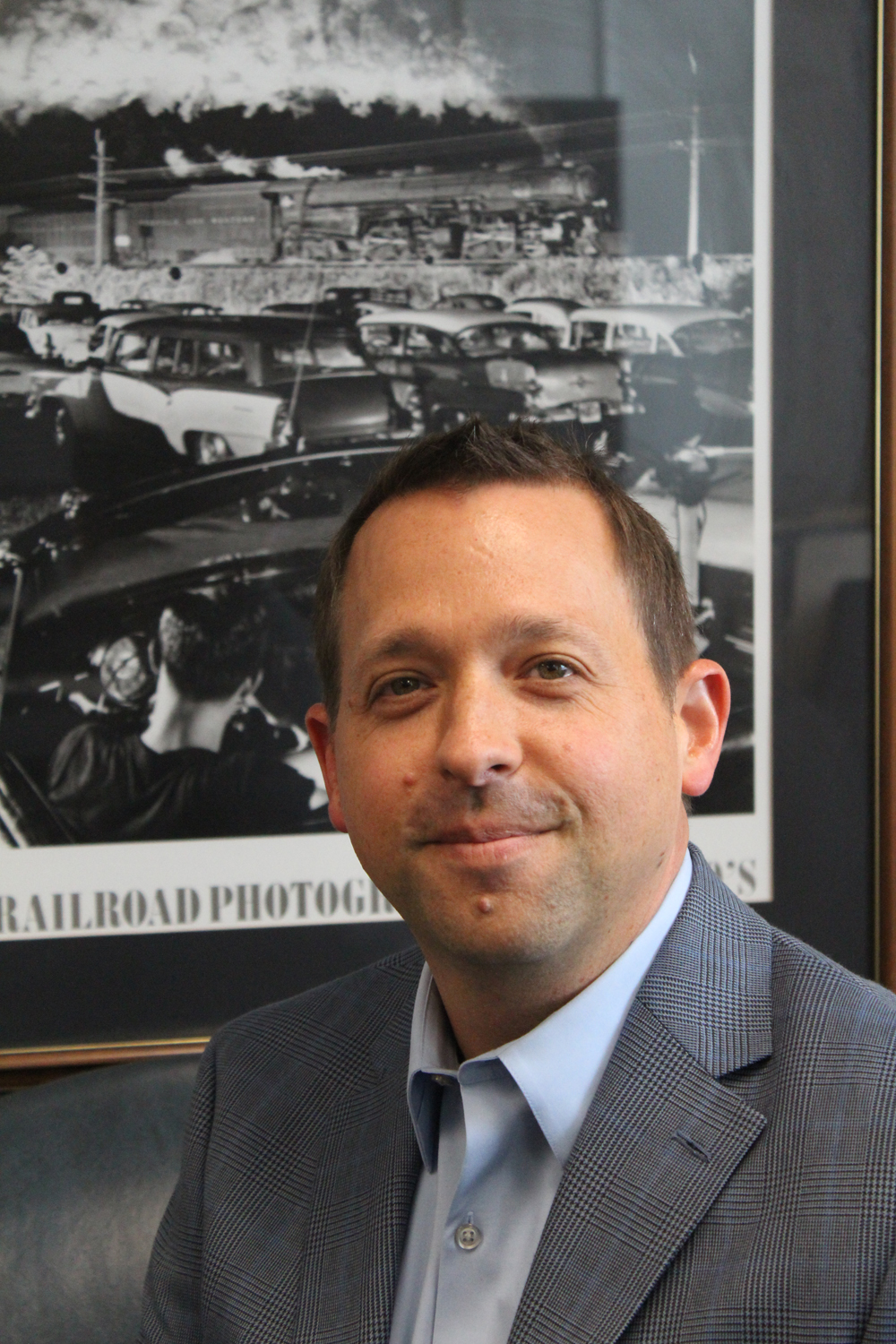 man in suit smiling in front of photo