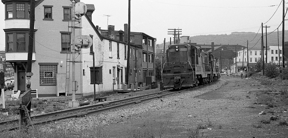 black and white photo of train by old buildings
