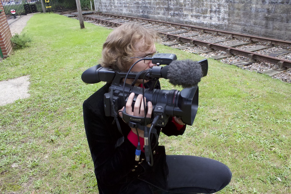 Camera man filming with train tracks in the background.