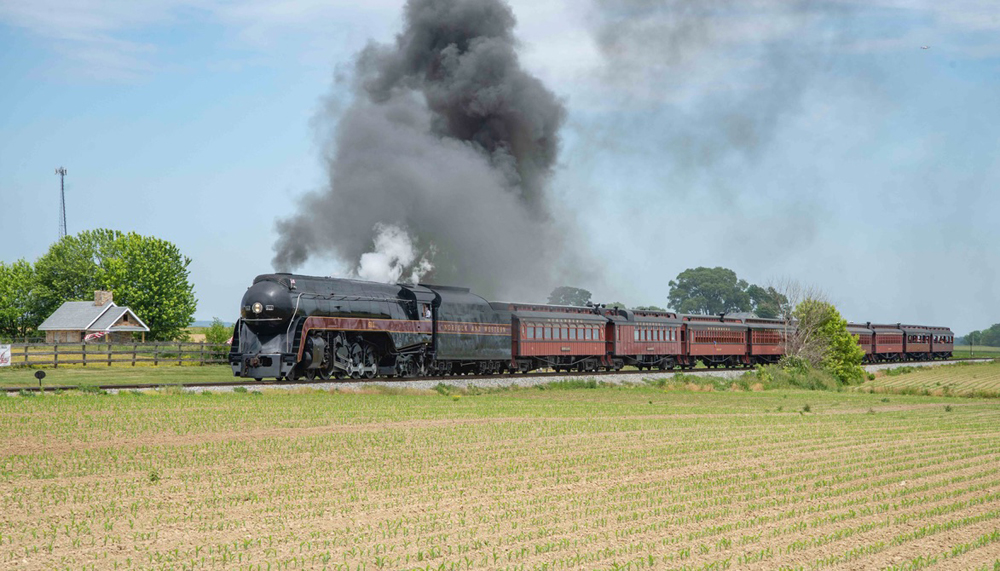Streamlined steam locomotive with train passes through field