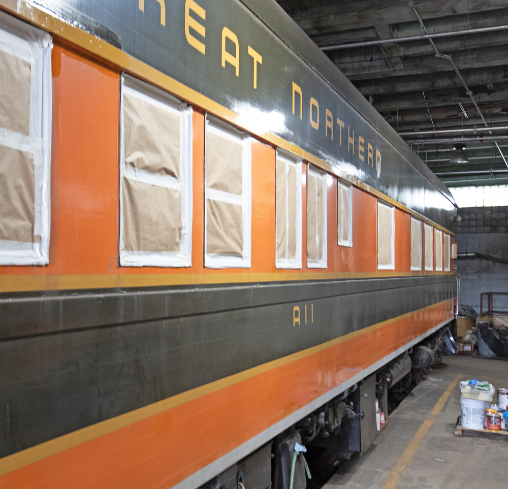 Orange and green passenger car in building with windows masked off for repainting