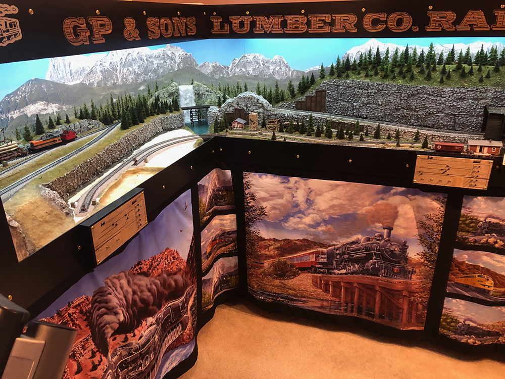 Jean Levasseur’s GP & Sons Lumber Co. in HO scale: model train set in L shape along two walls with black top and bottom and model trees and mountains