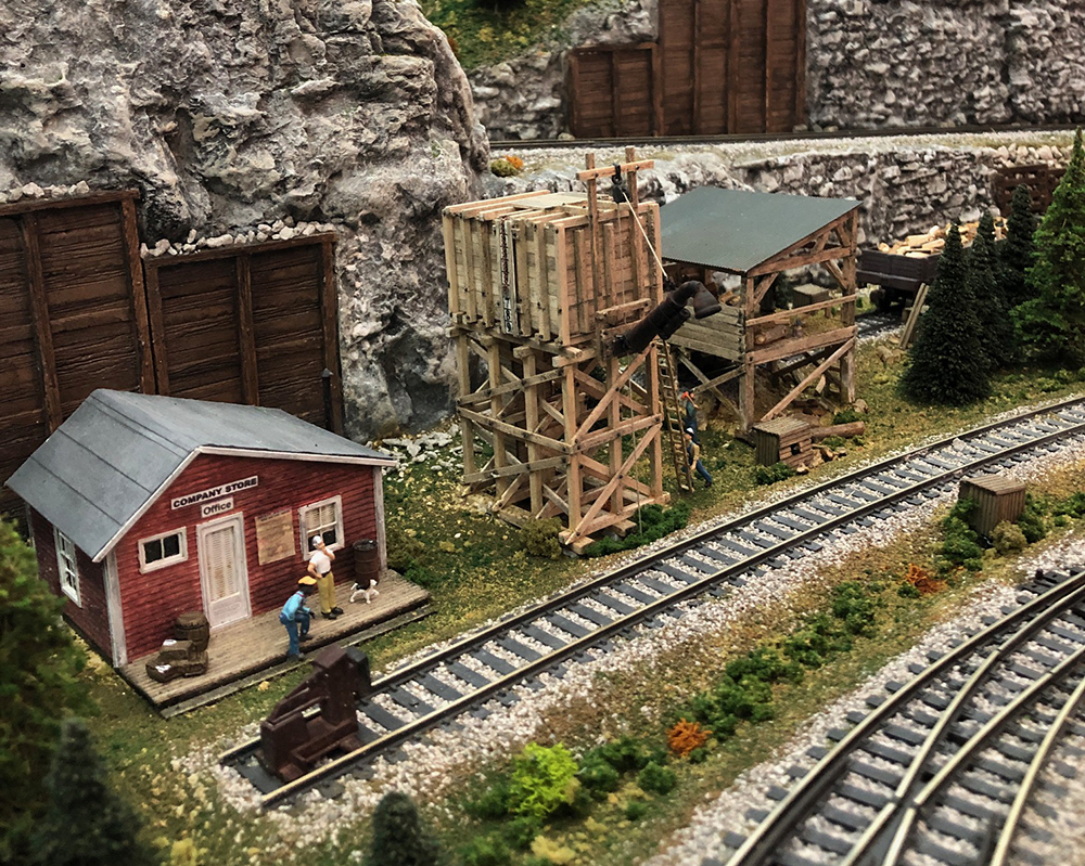 Model train buildings made of wood, including a square water tower and a small red office building