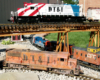 red, white, and blue diesel engine on trestle with faded orange diesel below on track

