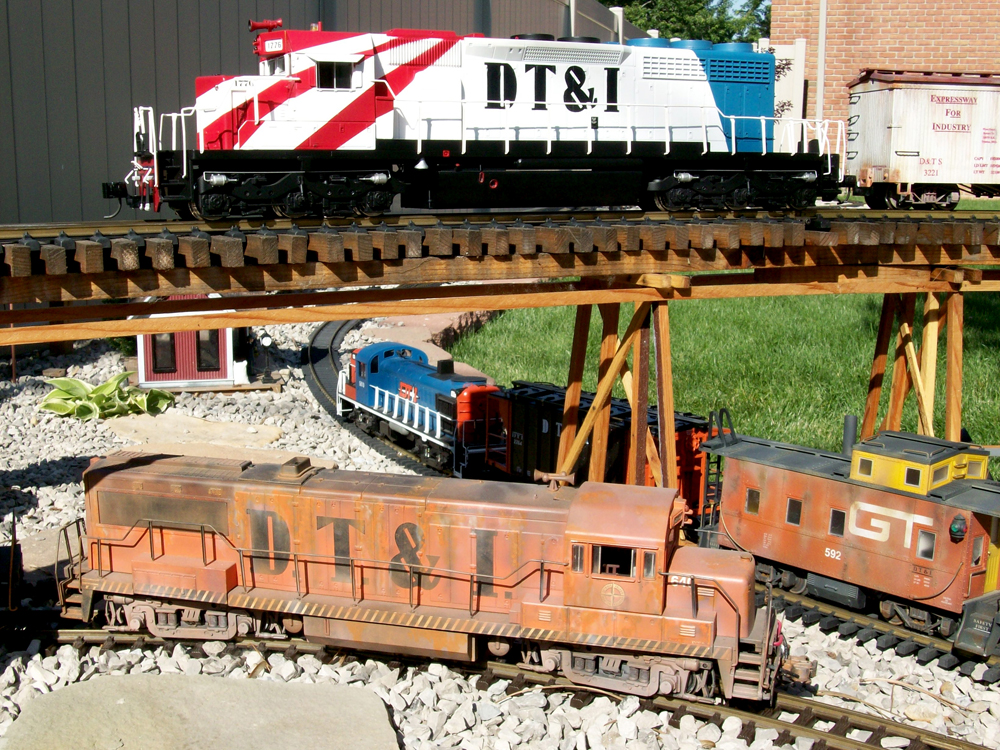red, white, and blue diesel engine on trestle with faded orange diesel below on track