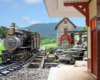 model steam locomotive approaches station on garden railway with blue sky in background