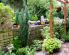 scene on garden railway with greenery, pergola, and a stone retaining wall