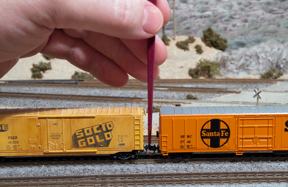 A hand uses a red plastic pick to uncouple two N scale freight cars