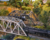Two steam engines pass each other on two steel truss bridges that span the same creek