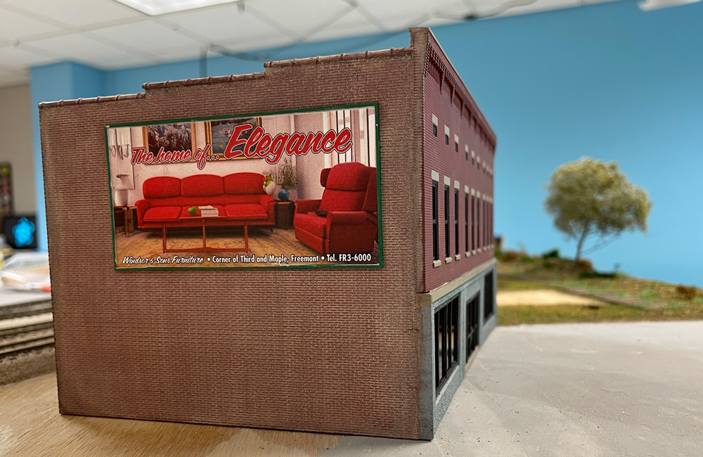 An HO scale brick building with a billboard for a furniture store on the side