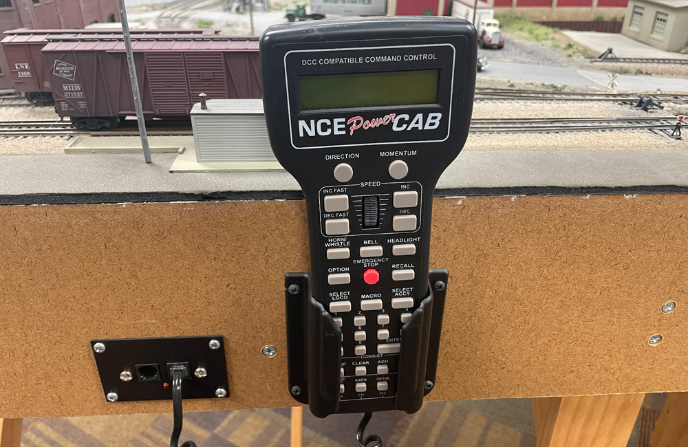 A model railroad throttle rests in a plastic holder on a layout fascia