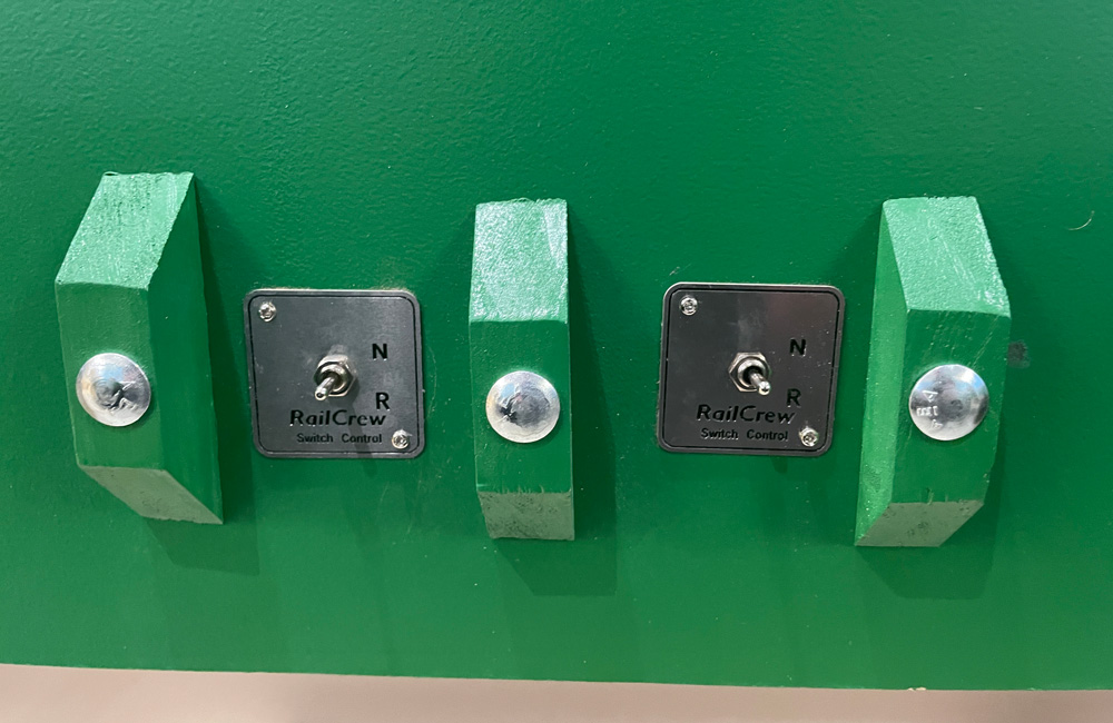 Two toggle switches on a green background, flanked by green wooden bumpers