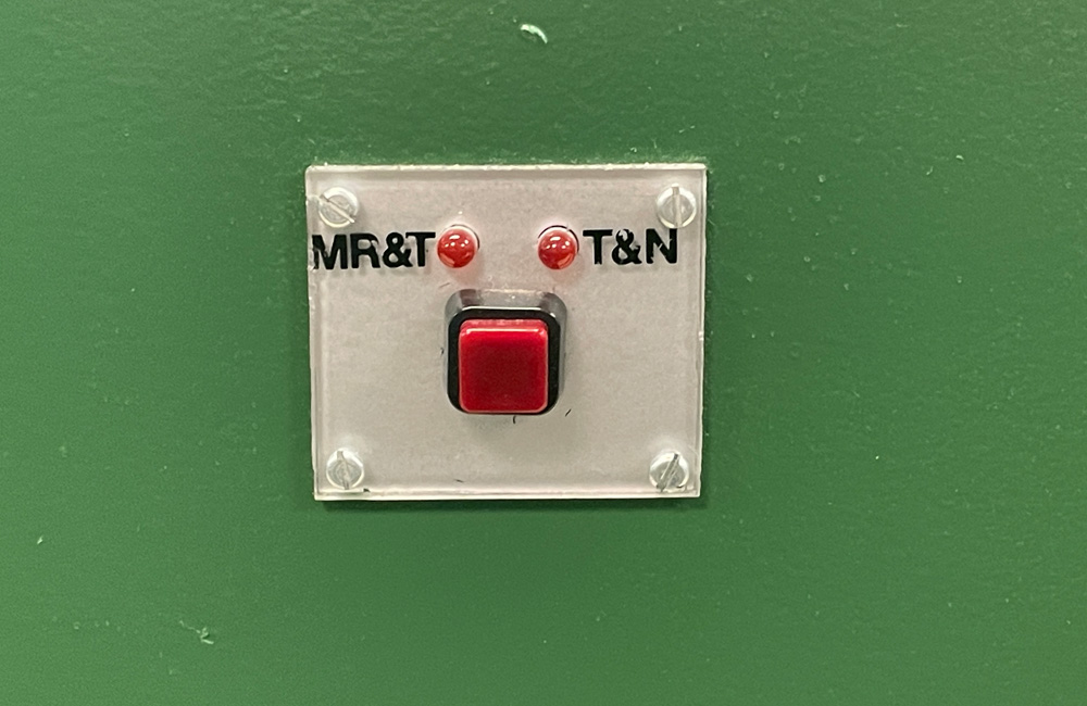 A red pushbutton is mounted beneath two red LEDs labeled MR&T and T&N