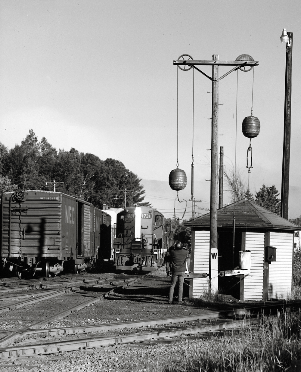 A man reaches to pull down a ball signal as a diesel locomotive approaches.