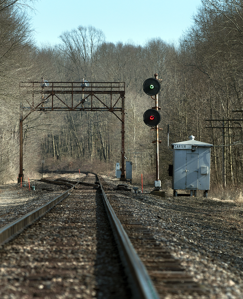 Track runs off into the distance with a switch to the left for a siding as a searchlight signals shows a green light above a red light.