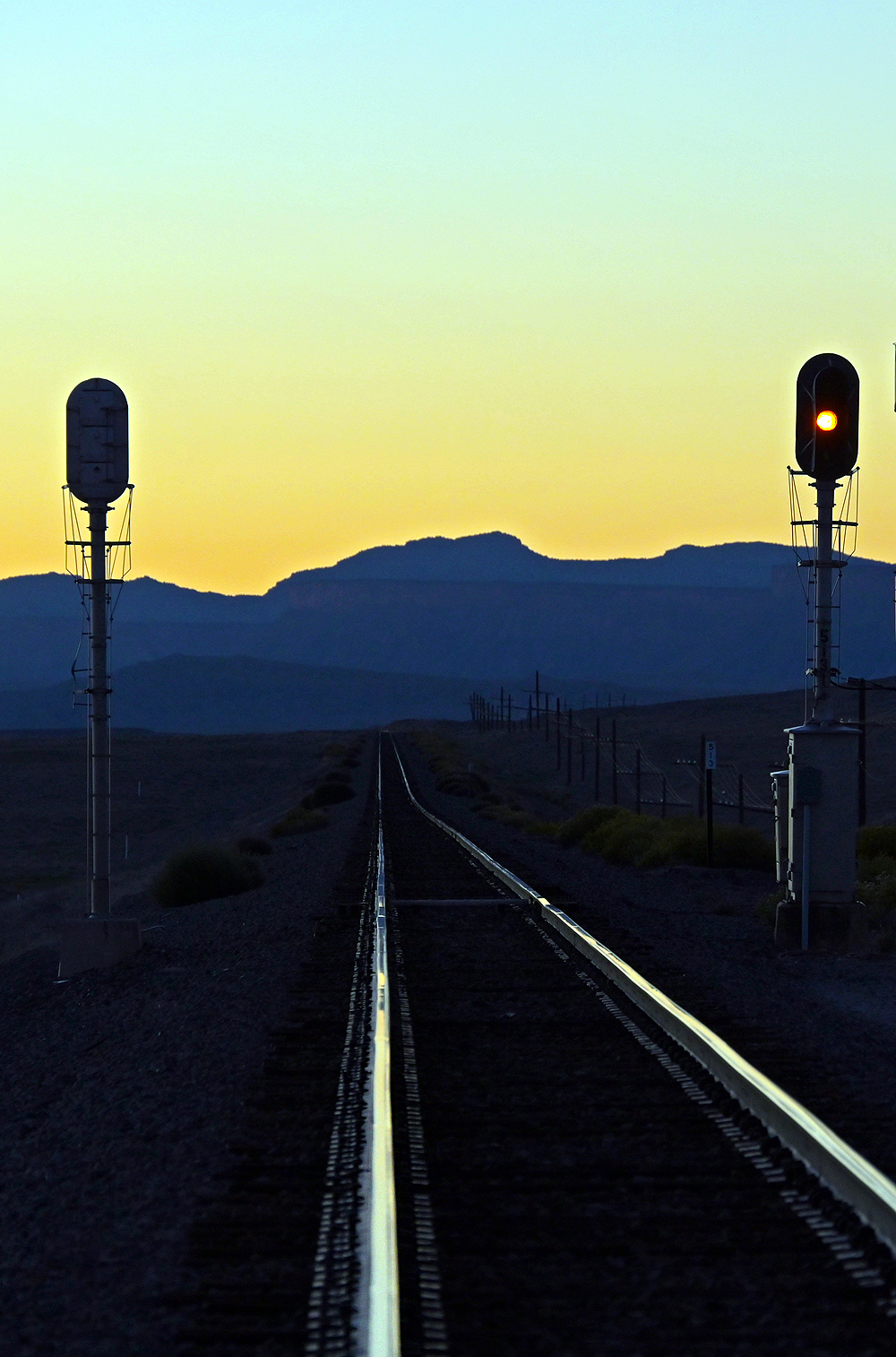 Color light signals are silhouetted against a desert sky with a mountain in the background.