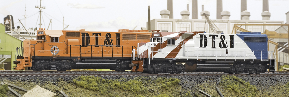 Color photo of two HO scale locomotives on scenic base with industrial backdrop.