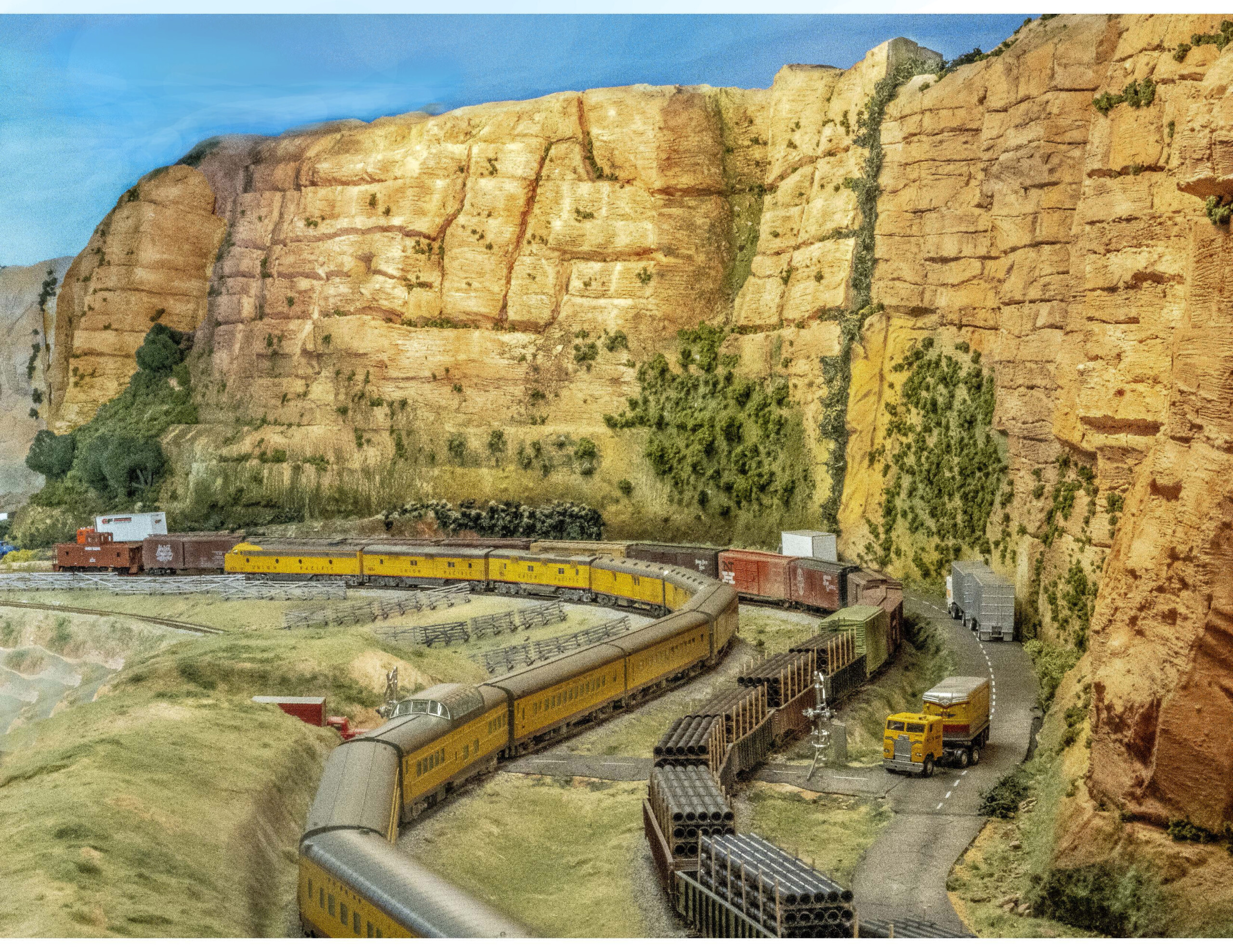 Two trains pass each other in a valley with a large cliff face in the background