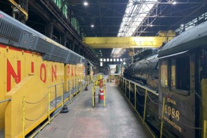 Yellow diesel locomotive and steam locomotive inside shop building