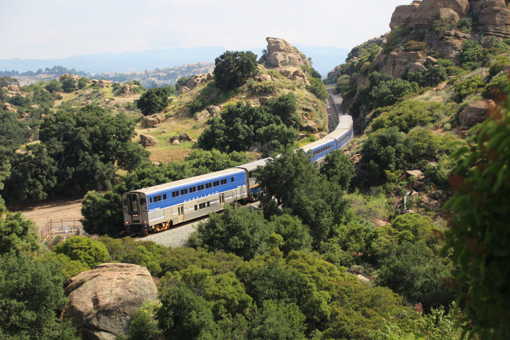 Passenger train with cab car leading passing through rocky hillside