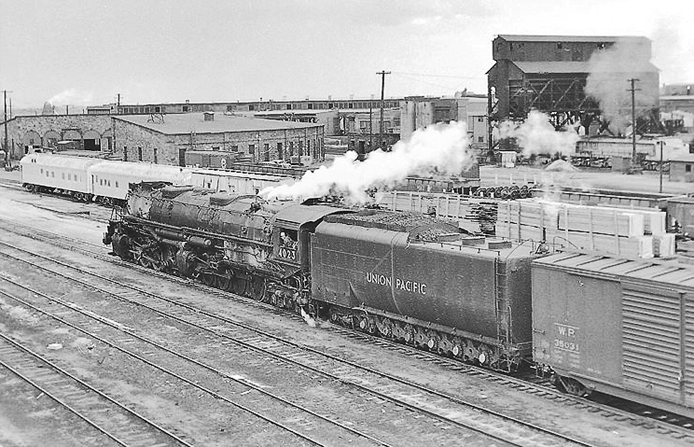 Black and white photo of a large black steam locomotive pulling a train through a freight yard. More of the Big Boy story