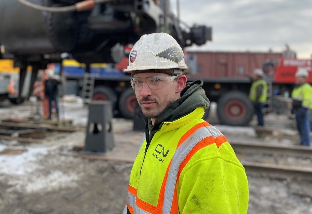 Portrait shot of young railroad worker in front of a steam locomotive.