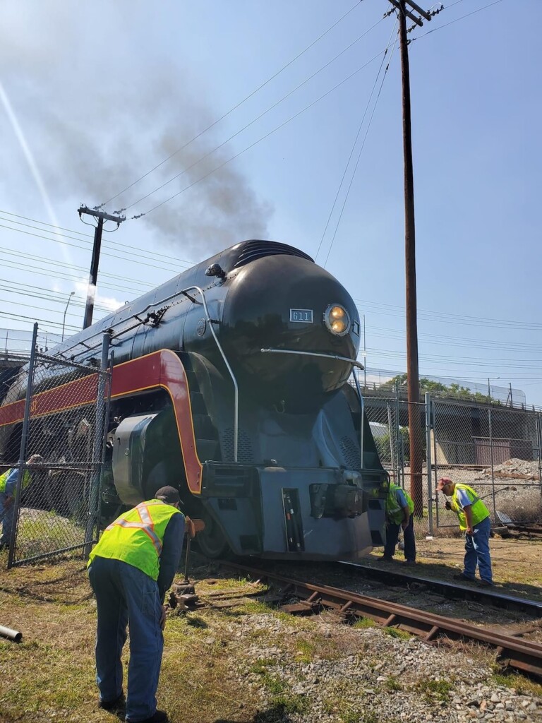 Steam locomotive pulls into yard while crew watches