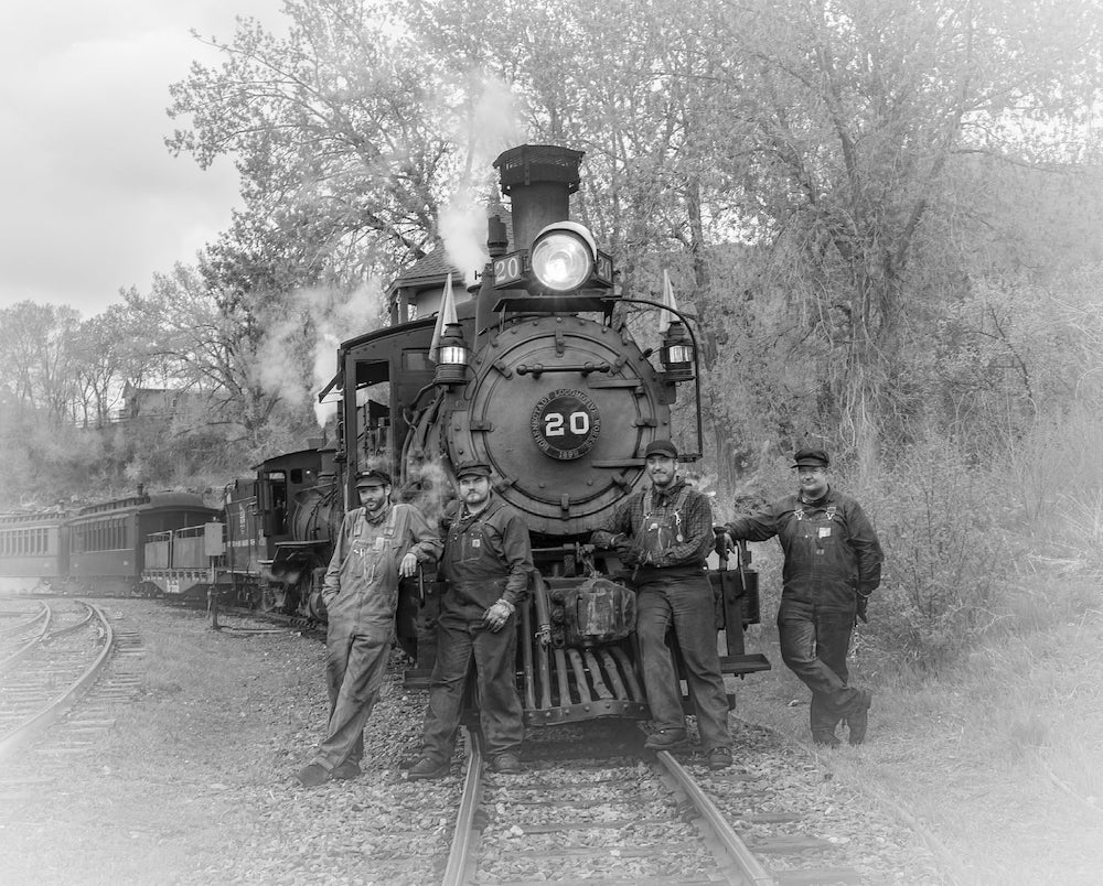 Black and white group photo in front of narrow-gauge steam locomotive.