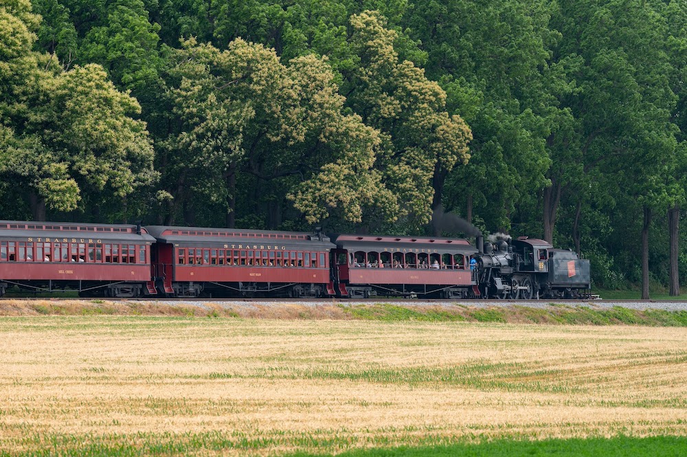 Steam locomotive pulling wooden passenger cars tender first.