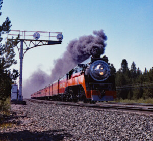 Black, orange, and vermilion steam locomotive pulling passenger train