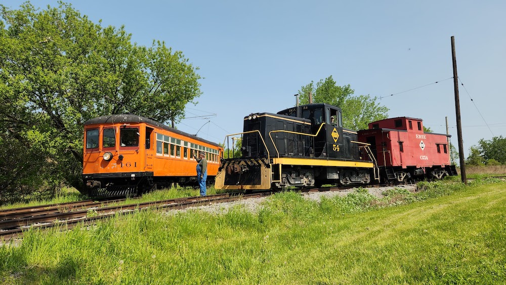 A trolley sits next to a diesel switcher coupled to a caboose.
