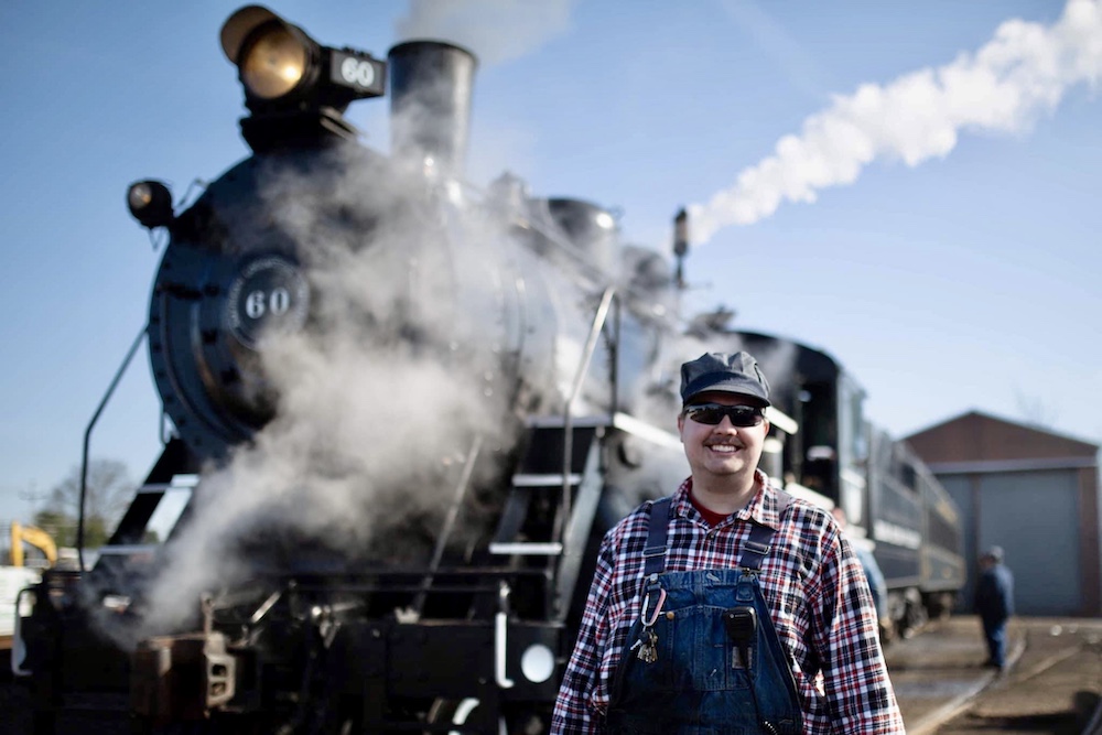 Young crew member posing in front of steam locomotive.