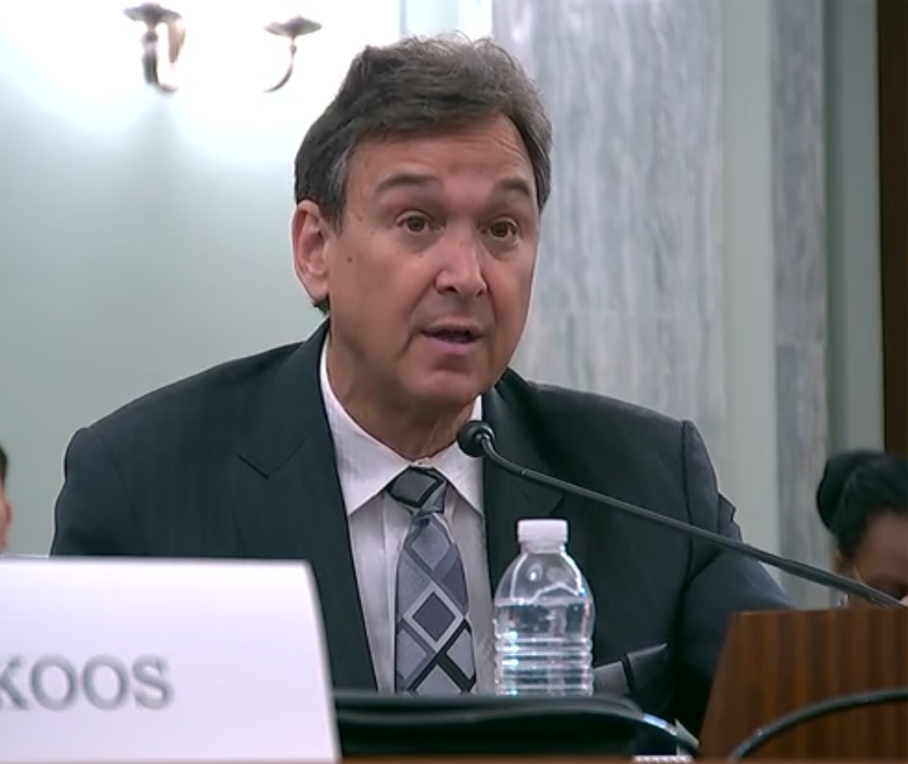 Man in suit speaking into microphone at hearing-room table