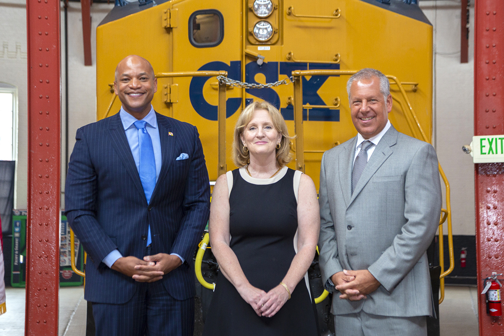 Three people pose in front of CSX locomotive