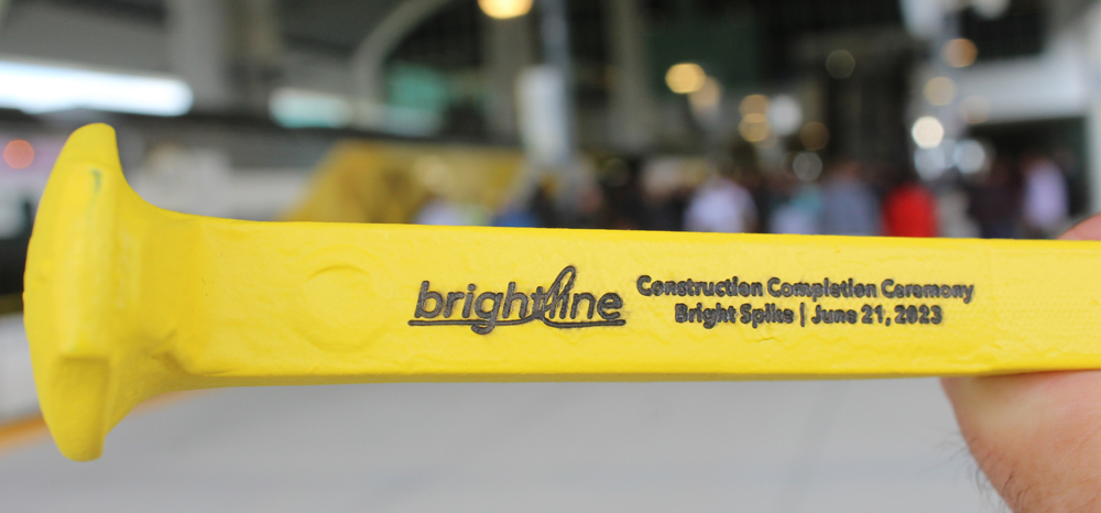 Yellow railroad spike with engraved message marking date of Brightline completion ceremony