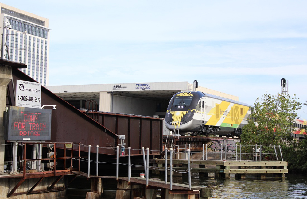 Passenger train approaches bridge; message board on bridge alerts boaters bridge is down for approaching train