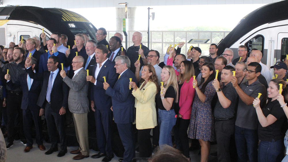 Large group of people standing in front of two locomotives holding yellow railroad spikes