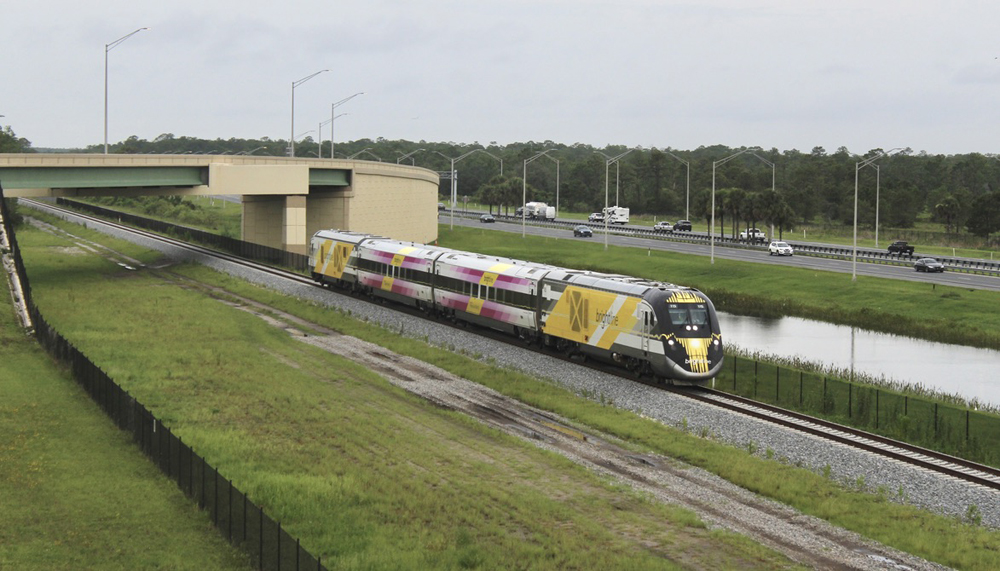Train with two locomotives and two passenger cars on straight track near road overpass