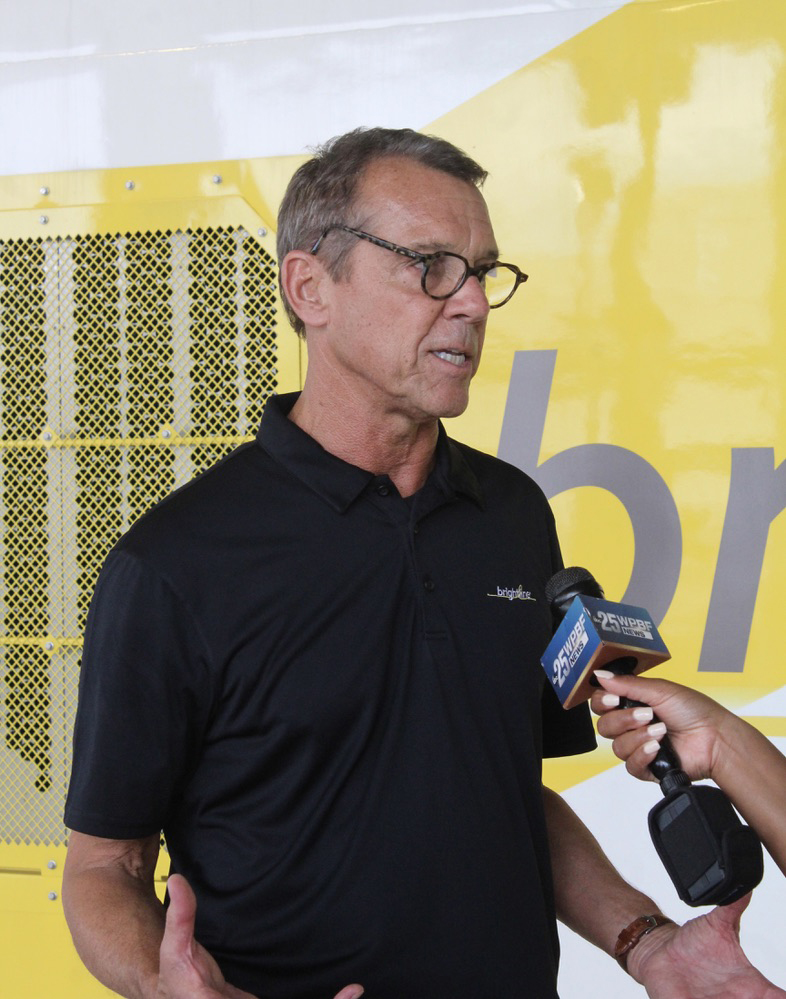 Man in black polo shirt being interviewed while standing in front of locomotive