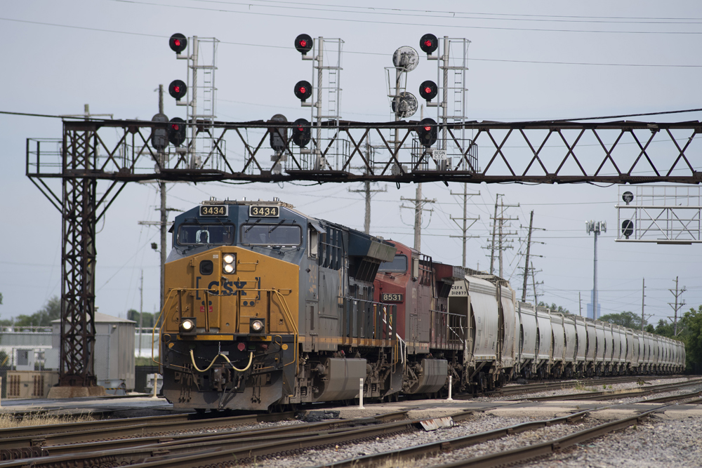 Blue and yellow locomotive and red locomotive on freight train passing under signal bridge