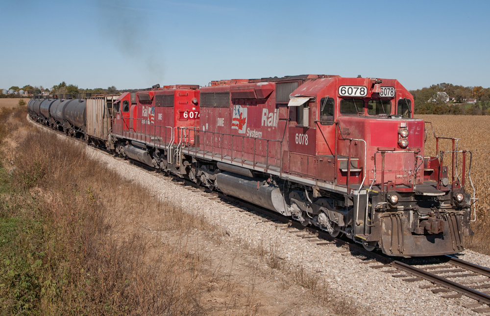 Two red locomotives leading freight train in flat territory.