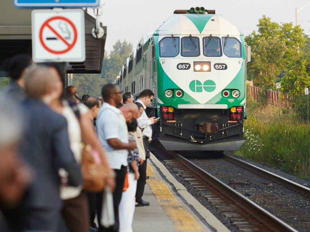 Green and white commuter train approaches crowded platform